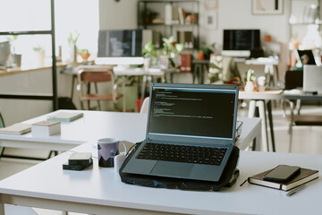 High angle shot of deep blue laptop with codes on cooling pad located in center of work desk with office supplies and smartphone