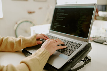 Medium close up of unrecognizable female hand with gold ring typing codes on laptop located on...