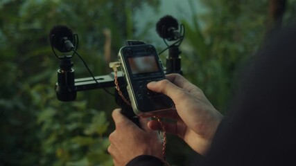 A young man is holding a microphone amidst a serene forest setting, surrounded by nature