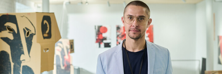 Panoramic of young male manager or owner of modern art gallery looking at camera while meeting new guests