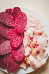 Sliced smoked sausage and bacon pieces close-up on light background.