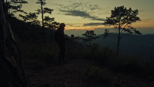 A young man holds a microphone to record his surroundings against the backdrop of a mountain sunset
