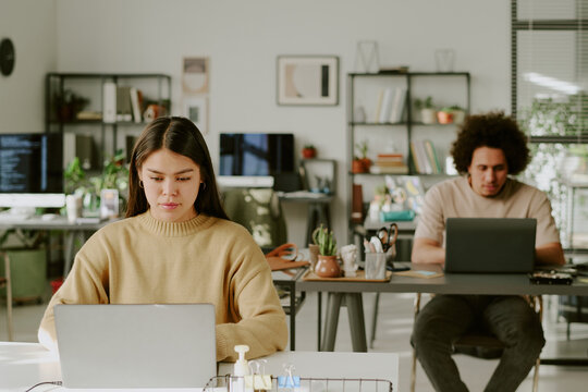 Biracial coworkers sitting at work desks and programming in modern office of IT company equipped with digital devices and extra workspaces