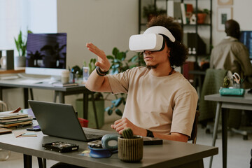 Men with VR headset testing new application and gesticulating wildly while sitting at work desk in...