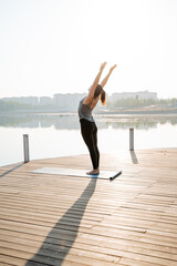 At dawn, a woman practices yoga at a tranquil dock, embodying wellness and mindfulness, harmonizing...