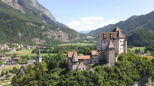 Gutenberg castle in Burg Gutenburg overlooking the town of Balzers in Liechtenstein, surrounded by mountains and greenery on a clear sunny day, drone pulling out shot