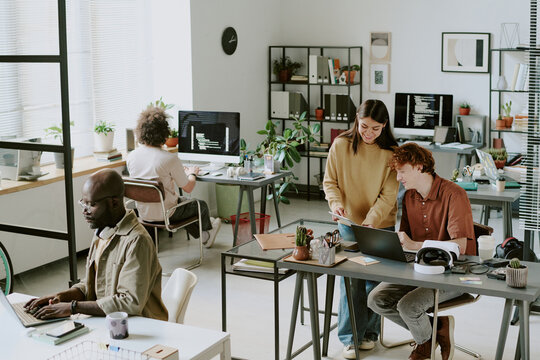High angle shot of cozy office full of digital devices and furniture, biracial workers interacting with each other and working