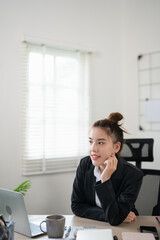 Thinking young asian business woman using laptop while sitting at desk at the office. Executive businesswoman wearing black suit.