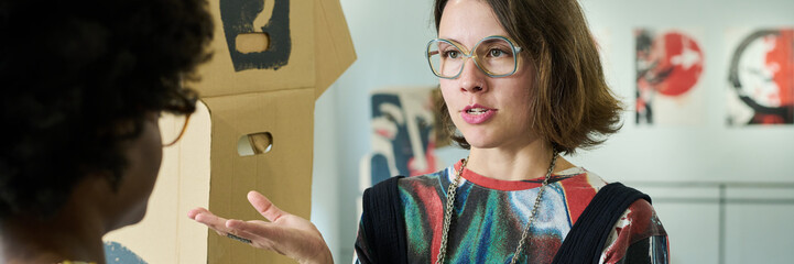 Banner of young brunette woman in eyeglasses explaining her opinion about represented artworks to...