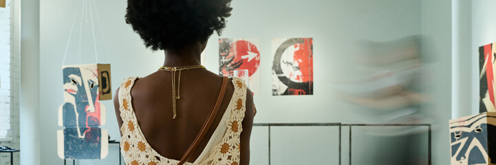 Banner of back of young African American female visitor of vernissage wearing elegant apparel standing in spacious gallery hall