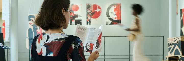 Header of young woman with dark straight hair looking through information about exhibition events...