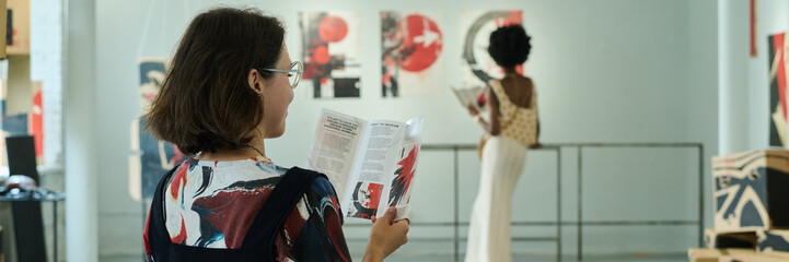 Panoramic of young female visitor of modern art gallery sitting in spacious hall and looking...