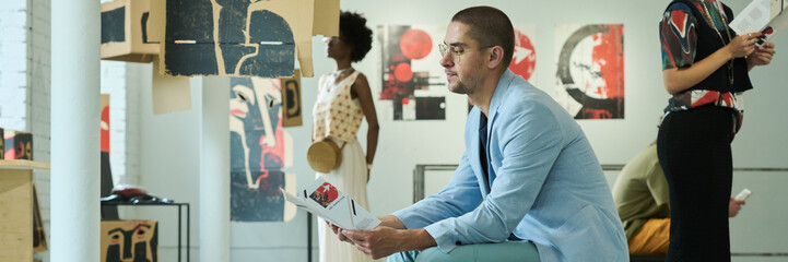 Banner of young male visitor of modern art exhibition looking through list of expositions represented at vernissage