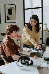 Obraz premium Vertical shot of young adult brunette female developer pointing at laptop screen while her coworker looking at it thoughtful