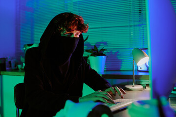 Medium close up ref curly haired man wearing black mask to hide his face sitting at table and...