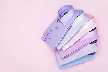 A pile of multi-colored folded shirts on a pink background with copy space, top view