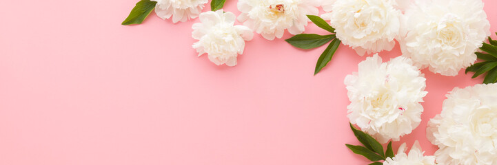 Fresh beautiful soft white peony flowers with green leaves on light pink table background. Pastel color. Closeup. Empty place for inspirational text, quote or sayings. Wide banner. Top down view. © fotoduets
