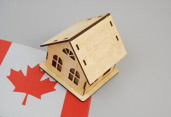 Wooden house on Canadian flag on gray background. Real estate in Canada concept.