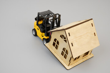 Obraz premium Yellow forklift truck and wooden house model on gray background 
