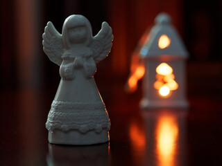 
The photo shows a white ceramic angel figurine in the foreground, with warm, soft lighting. In the blurred background, a glowing lantern creates a cozy, festive atmosphere. The focus emphasizes the 
