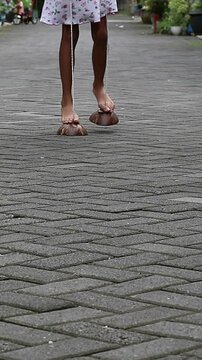 An unrecognizable Indonesian girl uses a coconut shell as a egrang stilt, traditional Indonesian games. A little girl balances on a coconut shell stilt, a symbol of childhood joy