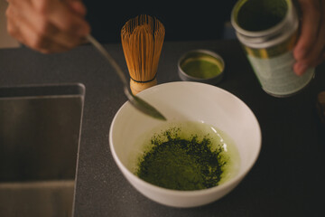 Woman adding matcha powder into bowl. Girl make atcha tea latte in the kitchen. Close up. Image matcha tea powder pouring in bowl. Japanese green tea concept.
