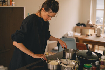 Beautiful happy young woman is cooking in the home kitchen and make meal from the pan on the stove. Turn on plate, stir the food.