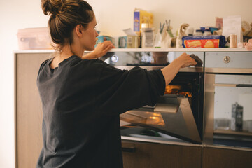 Young woman putting marinated chicken in oven. Girl turn on oven. 