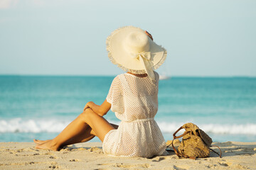 Beautiful slender woman in a white beach dress and hat stands on the seashore
