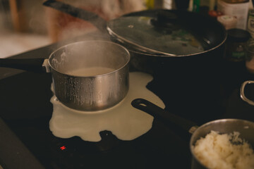 On the stove is a dirty saucepan stained with spilled milk. Cooking and burnt spots of escaped milk. 