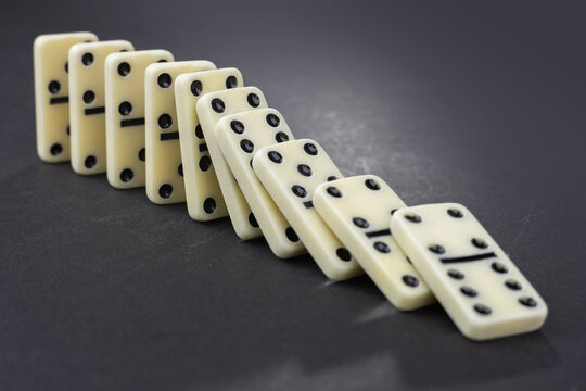 Domino effect concept with white dominoes pieces row falling on dark background.