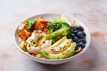Balanced vegan bowl with baked sweet potato, avocado, berries, salad and hummus. Plant Based Diet Concept.