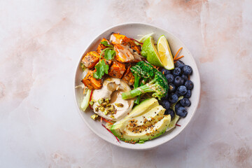 Balanced vegan bowl with baked sweet potato, avocado, berries, salad and hummus. Plant Based Diet Concept.