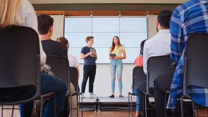 Two College Students Giving Presentation To High School Or University Class In Front Of Screen