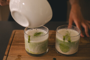 Close up two glasses with green matcha latte tea on wood board deck. Preparing matcha with milk.