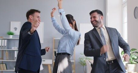 Team of business people having a party at work. Group of three happy coworkers dancing together. Two men and one woman celebrating success and having fun in the office