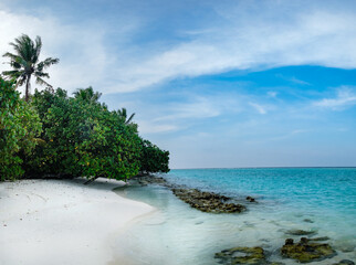 White sand sea beach panorama scenery with hot summer day in beautiful tropical paradise. Calm panoramic coastline landscape with exotic green trees and blue water waves, lagoon and clouds in sky