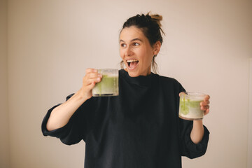 Happy woman hold two glasses of green matcha latte tea, wow emotions, lets drink tea together. Girl...