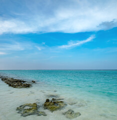 Tropical beach paradise, turquoise waves and ripples texture to horizon, coast rocks in shallow water. Summer calm coastline landscape with exotic lagoon, vacation and tourism simple scenery