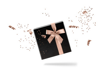 Black gift box with copper golden ribbon and confetti flying isolated on white background. Black...