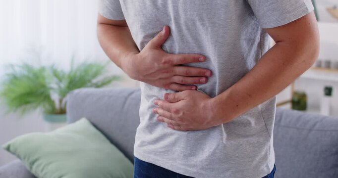 Man having pains in stomach. Young man suffering from a belly ache. Cropped shot of a sick man with an ulcer, IBS, colitis, or dyspepsia holding hands on his abdomen. Health problems concept