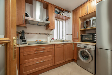 L-shaped fitted kitchen with cream stone effect worktop, stainless steel appliances and cherry wood cabinets