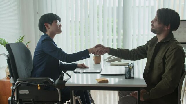 Side view of female Asian entrepreneur in officewear shaking hands with young man during job interview at office
