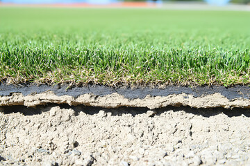 Cross-section of artificial turf revealing its layers grass, adhesive, and base. Ideal for landscaping, sports field construction, and gardening projects.