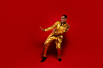 Charismatic young man in a shiny golden suit poses against a vibrant red background, exuding...