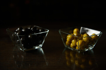 Black and green olives in glass bowls on a wooden table