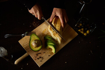 Cutting fresh bread and avocado on a wooden board in dim lighting