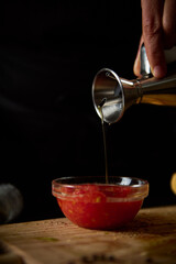 Pouring olive oil into a bowl of fresh tomato sauce on wooden table