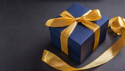 Elegant Dark Blue Gift Box Tied with a Luxurious Gold Satin Ribbon on a Dark Background Perfect for Birthdays and Special Occasions