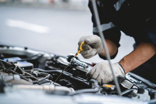 A mechanic is working on a car engine, checking the oil level and adding more if necessary. Concept of responsibility and attention to detail